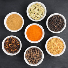 Spice green cardamom, red chili pepper, black pepper, fenugreek, cloves, allspice, masala powder in white ceramic bowl on black wooden background. Healthy eating and organic food concept