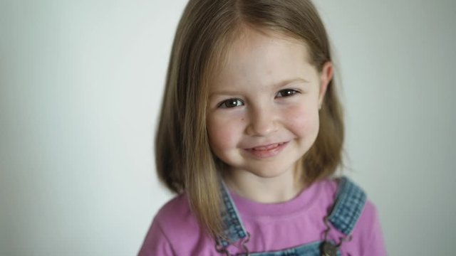 Preschool girl looks at the camera smiling, then resents crossing arms on her chest, close-up of little blonde cute girl’s face. Face portrait closeup.