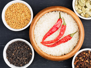 Basmati long, rice, black pepper, fenugreek, green cardamom, hot red chili pepper, cloves on black wooden background. Healthy eating and organic food concept