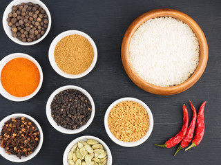Basmati long, rice, black pepper, masala powder, fenugreek, green cardamom, hot red chili pepper, cloves, tomato on black wooden background. Healthy eating and organic food concept