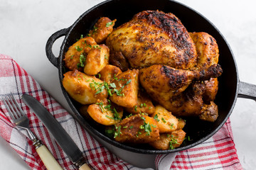 Baked whole chicken with potatoes and herbs in a rustic style. Top view, side view on a light background. Close-up and medium plan. Space for text.