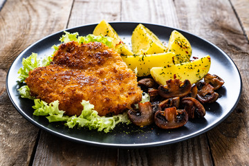 Schnitzel with boiled potatoes and fried champignon on wooden table