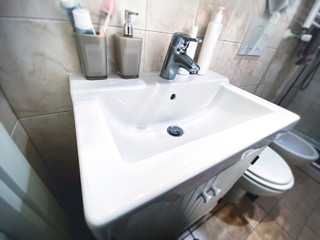 white sink with chromed steel tap inside a small bathroom of an apartment.