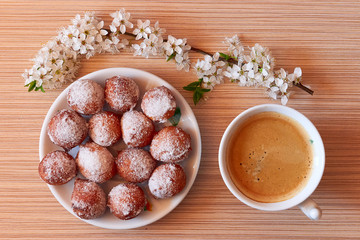 Starting morning with a coffee and homemade donut holes with a blooming brach on desk , during pandemic isolation