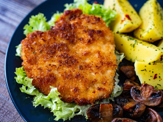 Schnitzel with boiled potatoes and fried champignon on wooden table