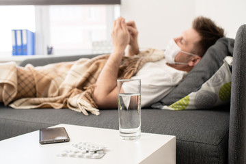 sick man lies under a blanket with a tablet. near a glass of water and pills
