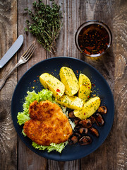 Schnitzel with boiled potatoes and fried champignon on wooden table
