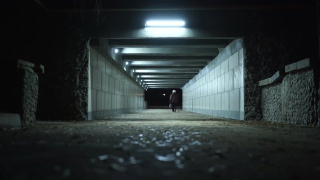 Woman walking through the pedestrian underpass tunnel passage at night.