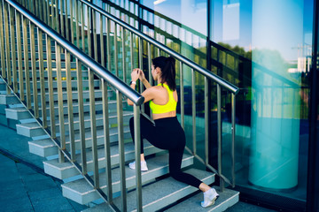 Fototapeta na wymiar Back view of slim caucasian female athlete in activewear having workout outdoors on stairs keeping healthy lifestyle, sports women with good physical strength and figure squatting during training