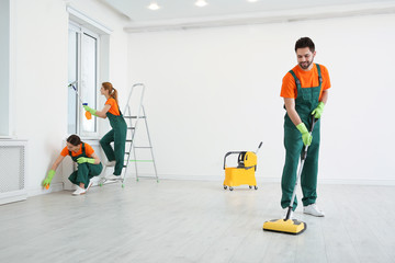 Team of professional janitors in uniforms cleaning room