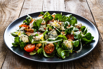 Fresh salad - blue cheese, cherry tomatoes, vegetables and walnuts on wooden background