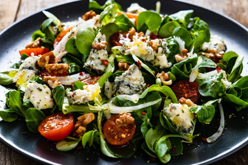 Fresh salad - blue cheese, cherry tomatoes, vegetables and walnuts on wooden background