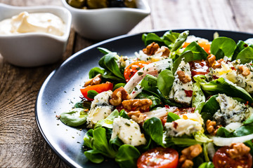 Fresh salad - blue cheese, cherry tomatoes, vegetables and walnuts on wooden background