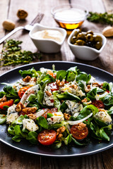 Fresh salad - blue cheese, cherry tomatoes, vegetables and walnuts on wooden background