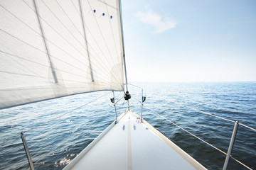 White yacht sailing on a sunny summer day. Top down view from the deck to the bow, mast and sails. Waves and water splashes. Clear blue sky. Gulf of Finland © Alex Stemmer