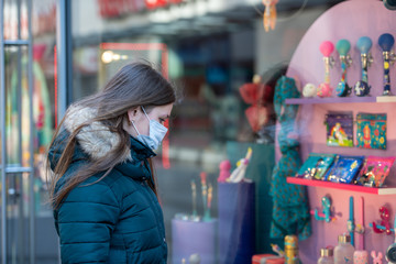 Fototapeta premium Young woman wearing medical protective mask in the front of clodes shop
