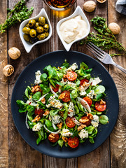 Fresh salad - blue cheese, cherry tomatoes, vegetables and walnuts on wooden background