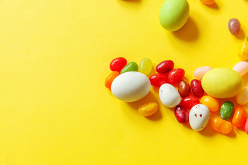 Happy Easter concept. Preparation for holiday. Easter candy chocolate eggs and jellybean sweets isolated on trendy yellow background. Simple minimalism flat lay top view copy space