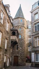 Fototapeta na wymiar Old stone tower in Saint Malo in French Brittany, stone construction with half-timbered balcony and white windows with old street lighting.