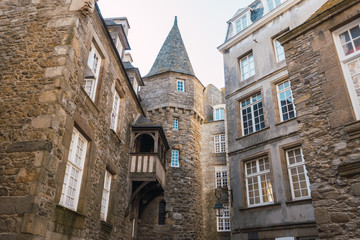 Old stone tower in Saint Malo in French Brittany, stone construction with half-timbered balcony and white windows with old street lighting.
