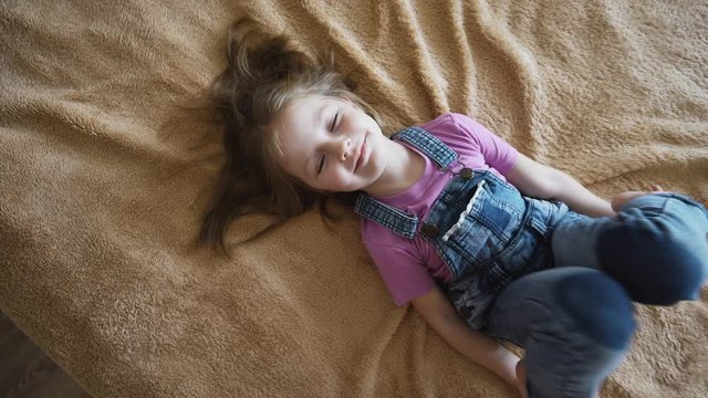Close-up high angle view of&nbsp;a blonde cute  preschool girl laying down&nbsp;on a bed covered with beige blanket at home. Closeup of baby&rsquo;s face portrait.