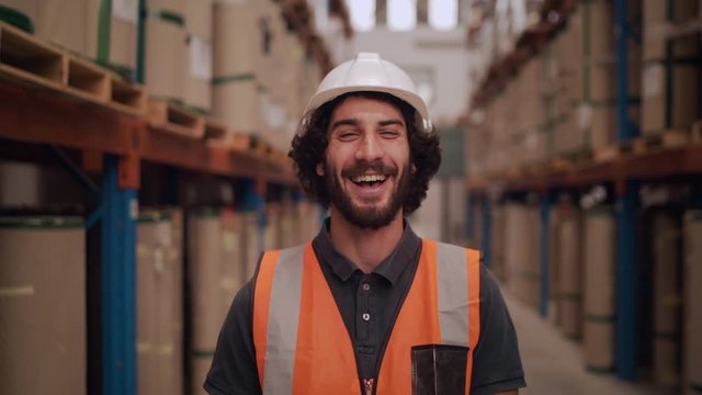 Portrait of a caucasian warehouse worker standing in large warehouse distribution center smiling and looking at camera