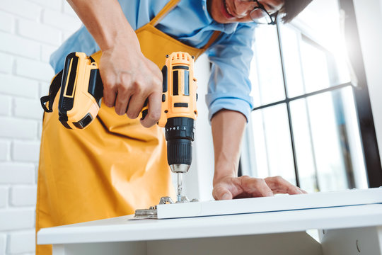 Happy Asian Man Home Improvement Assembling Furniture Reads Instructions And Tightens Screw With A Drill. Moving Into New House Renovation Concept