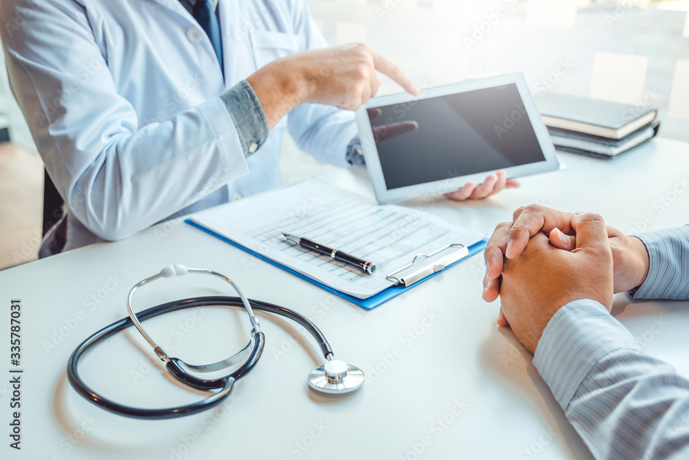 Wall mural doctor consulting with patient presenting results on digital tablet tablet sitting at table