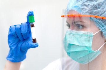 Woman in face mask and face shield checking test tube for testing blood for coronavirus. Concept empty lable test tube.