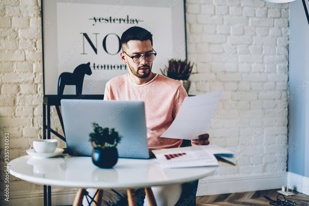 Poster pensive caucasian male businessman in eyewear checking documentation working from home remotely, 20s