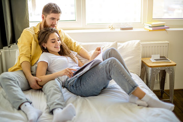 young caucasian married couple relax at home, enjoy being together, have rest lying on bed and reading a book. leisure time, weekends or holidays. indoors
