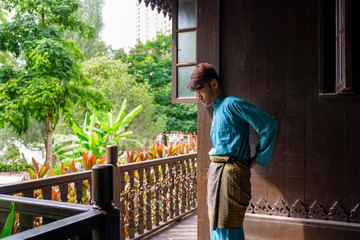 Malay man are wearing traditional cloth and adjusting his samping songket at traditional wooden house