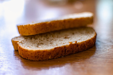 Two sliced slices of bran bread with a crisp crust of rye flour, lying on a brown wooden table, after fresh baking in the kitchen in the sunlight