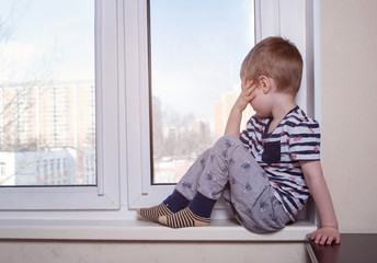 The boy is sitting on the window sill. Sad mood.