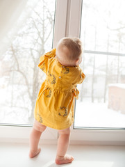   little girl of 9 months standing on   window sill .