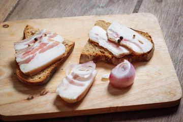 Lard sandwich with black bread and onions on a wooden board.