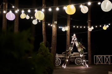 Wedding ceremony in the forest at night with Chinese lanterns. Triangular wooden arch.