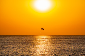 Silhouette of a parachute and a skydiver against the background of a bright burning sunset over the sea. A shining sun and an object flying in the yellow sky.