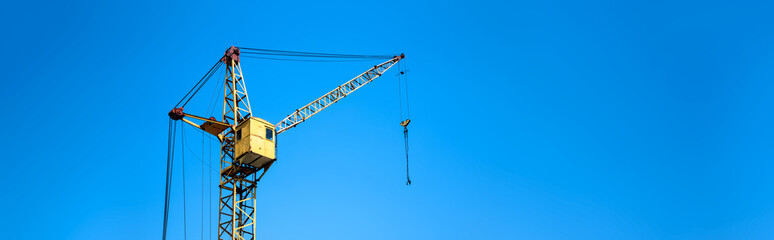 yellow construction elevator crane close-up against the blue sky, panoramic mock-up with space for...