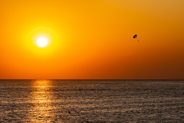 Silhouette of a parachute and a skydiver against the background of a bright burning sunset over the sea. A shining sun and an object flying in the yellow sky.