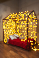 Bed in the form of a house with garlands in defocus. Background yellow warm collection of Christmas decorations. The bokeh from the lights in the bedroom