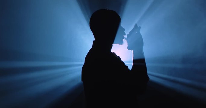 Profile of dark black silhouette of man posing and dancing in darkness space in light of single blue light. Profile of male moving hands in one lamp ray. Disco clubbing concept. Shadow dance Side view