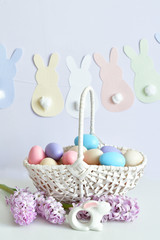 Colorful easter eggs in basket on pastel color background with flowers, copy space.Easter decorations. Easter background with painted eggs with Hyacinth, top view. Spring greeting card
