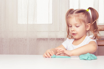 girl preschooler sits at a table and sculpts from turquoise dough for modeling. activities with children at home on self-isolation in connection with coronavirus infection