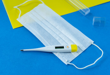 Thermometer and medical mask on a blue and yellow background