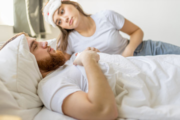Obraz na płótnie Canvas cute young caucasian woman look at sleeping man waiting when he wakes up. married couple on bed in the morning. weekend, holiday, morning at home