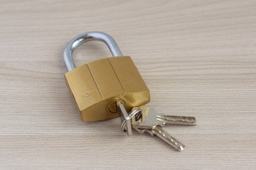 Closed padlock with keys in the keyhole on a light wooden background.