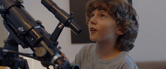 Curious Caucasian kid boy using telescope to explore moon surface. Stay home, learning from home,...