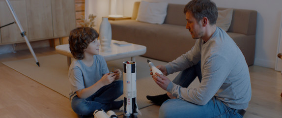 Caucasian father and son playing at home, building moon landing mission rocket together. Stay home,...