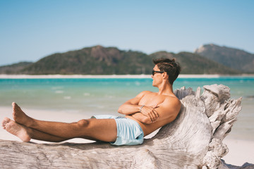 Fototapeta na wymiar Male model wearing sunglasses and fitness body on the beach posing